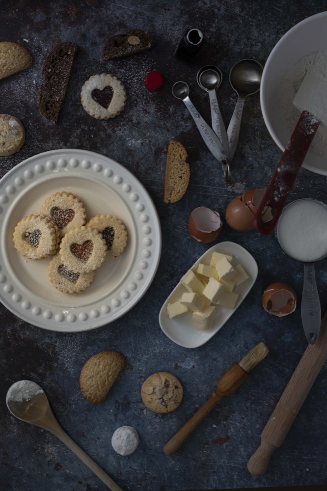 Overhead baker's table with linzer cookies, measuring spoons, butter, flour and cracked eggs