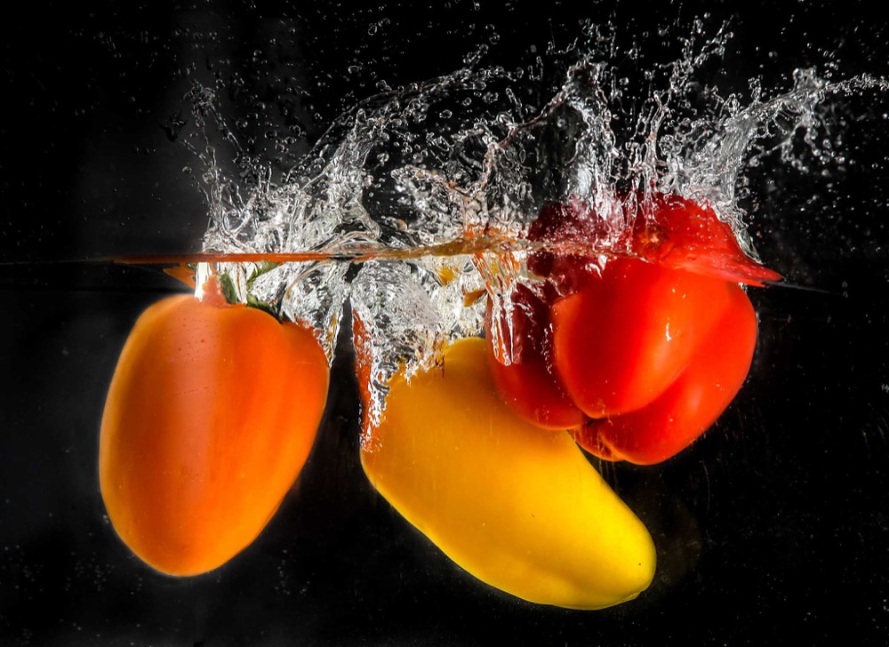 Red, orange and yellow peppers plunging into water with a burst of splash, on black