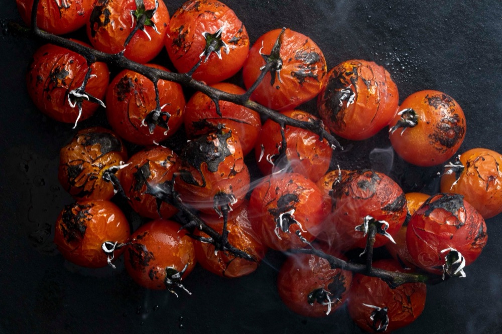 Fire-roasted cherry tomatoes on the vine with drifting smoke, on dark slate