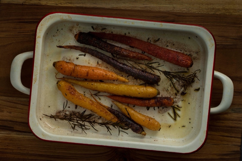Roasted heirloom carrots with rosemary in a white enamel roasting pan