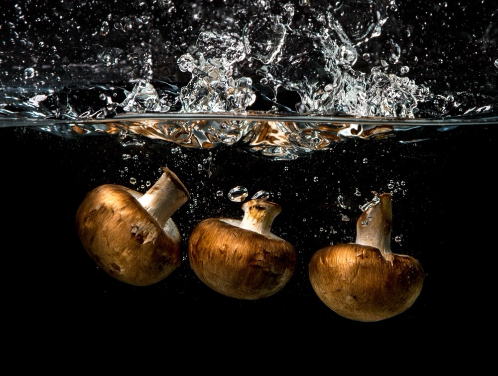 Three cremini mushrooms plunging into water with a crown of splash, on black