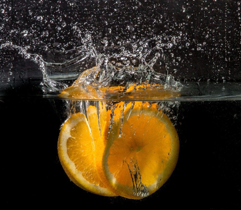 Orange slices dropping into water with an explosive splash, on black