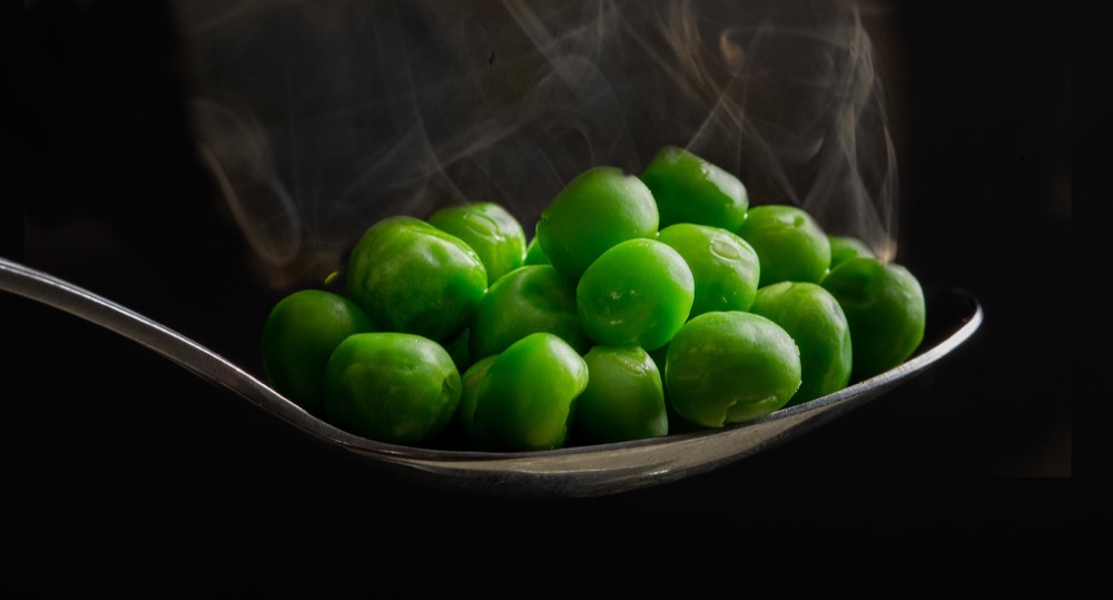 A spoonful of bright green peas with steam rising, against black