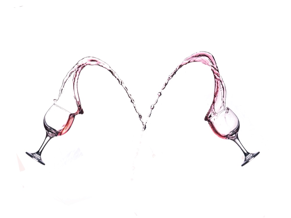 Two wine glasses throwing arcs of rosé that meet in the shape of a heart, on white