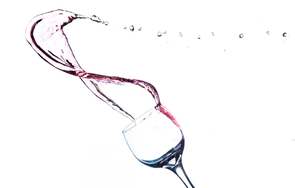 A single wine glass with a ribbon of rosé spiralling out of it, on white